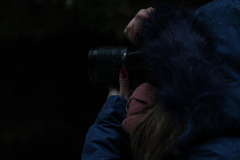 Photographie d'une femme de profil, le visage caché par une capuche bleue et un objectif d'appareil photo