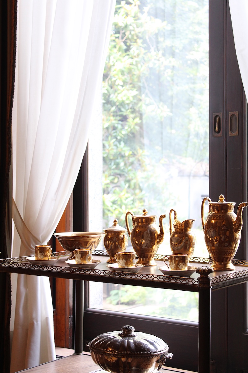 Photographie d'une table basse devant une fenêtre avec des théières et tasses en acier doré