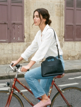 Une femme en jean et chemise blanche sur un vélo de ville, elle porte le sac LUA N°1.