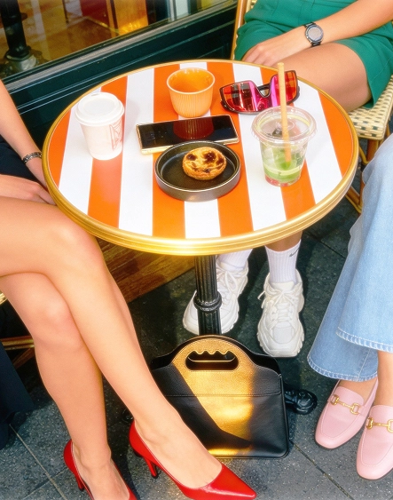 3 femmes assises en terrasse avec des boissons fraîches et un sac à main en synderme posé sous la table.